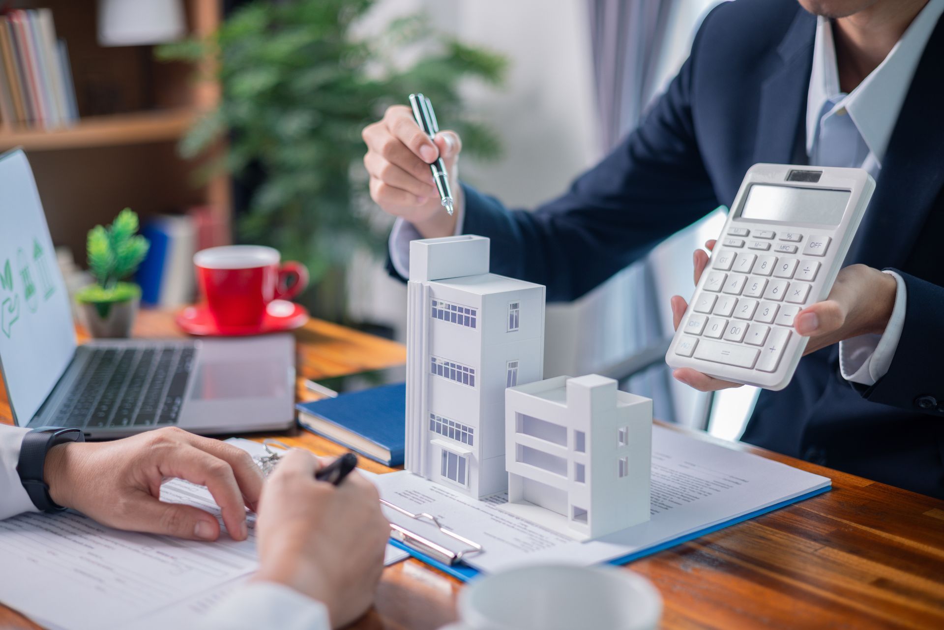 Business meeting with model buildings and calculator on a desk, discussing finances.