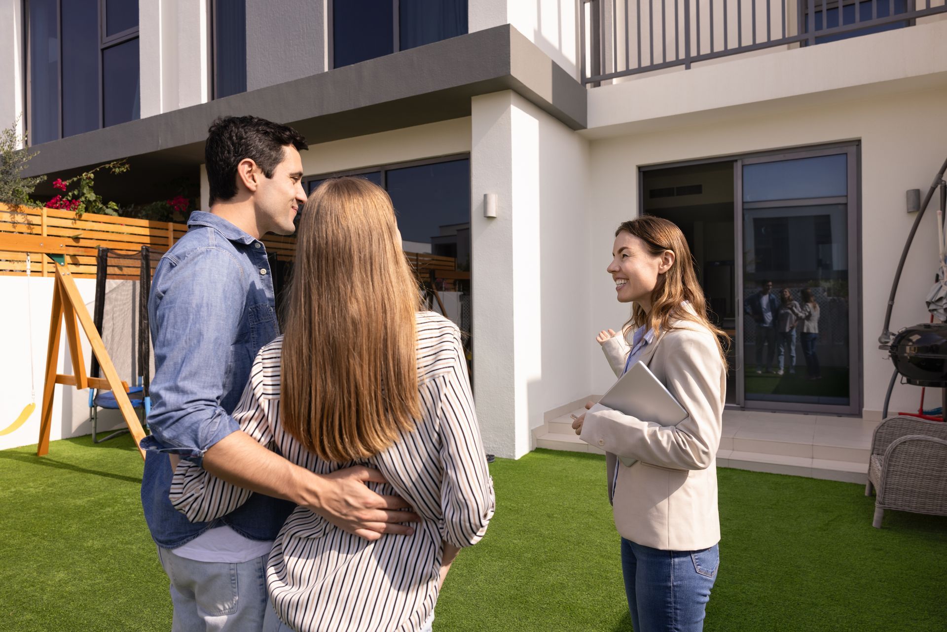 Three people talking outside a modern apartment building on a sunny lawn