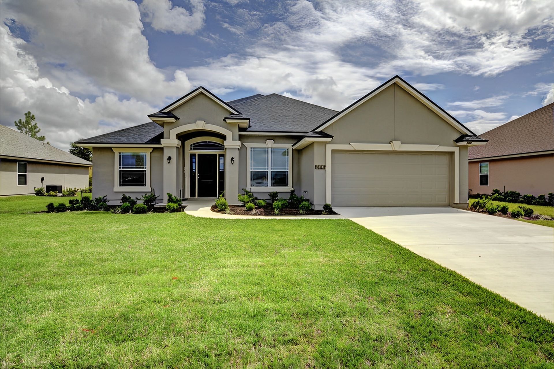 Suburban single-story house with a two-car garage, white exterior, and a green lawn under a cloudy sky