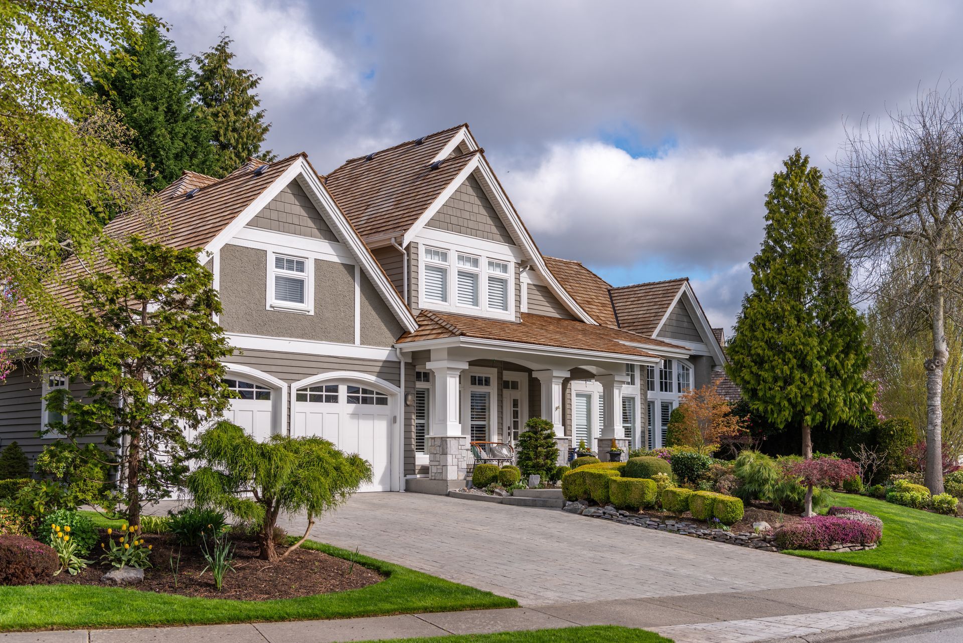Large gray suburban house with a manicured lawn, driveway, and landscaped front yard