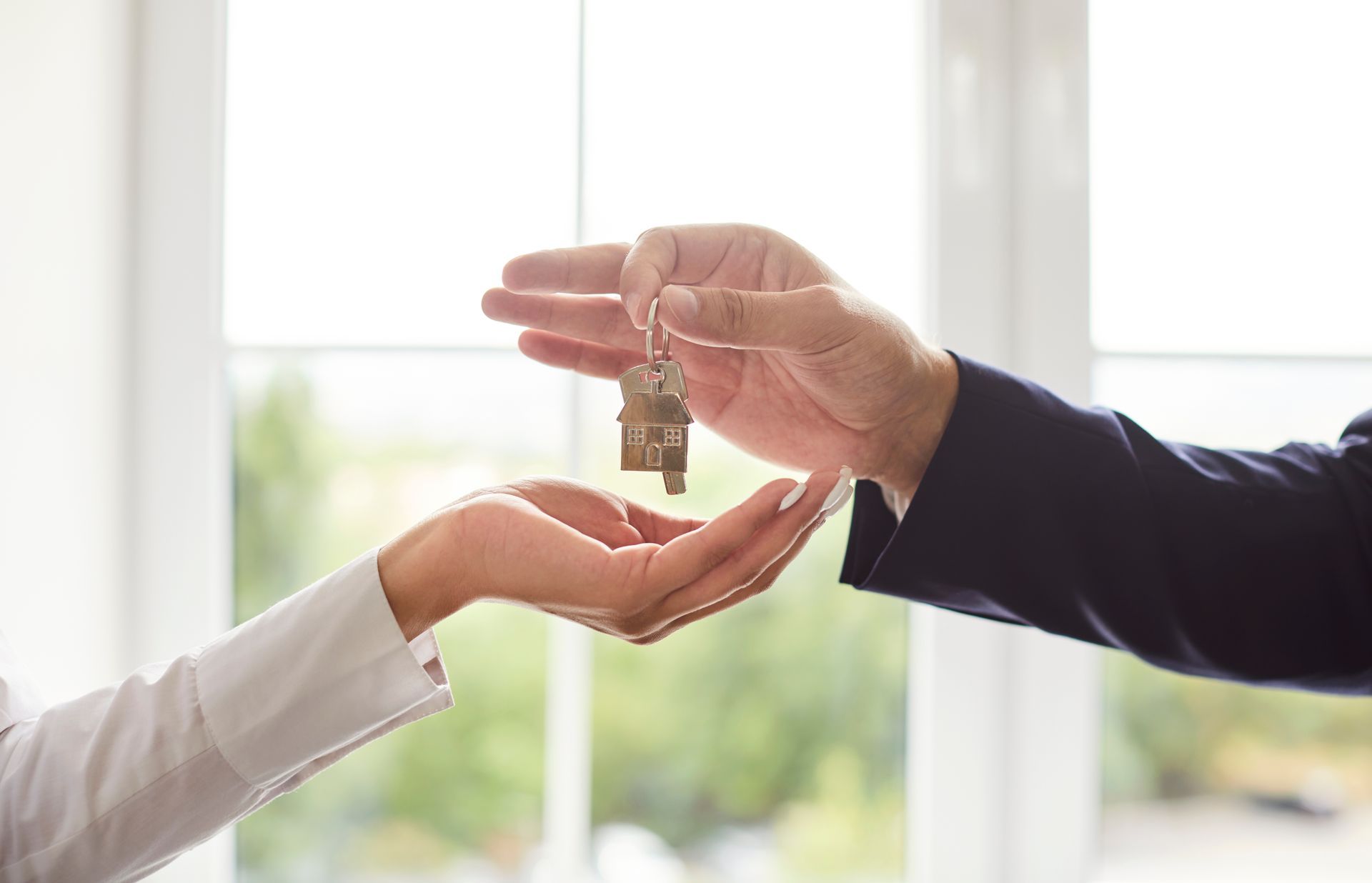 Hands exchanging house keys near a bright window