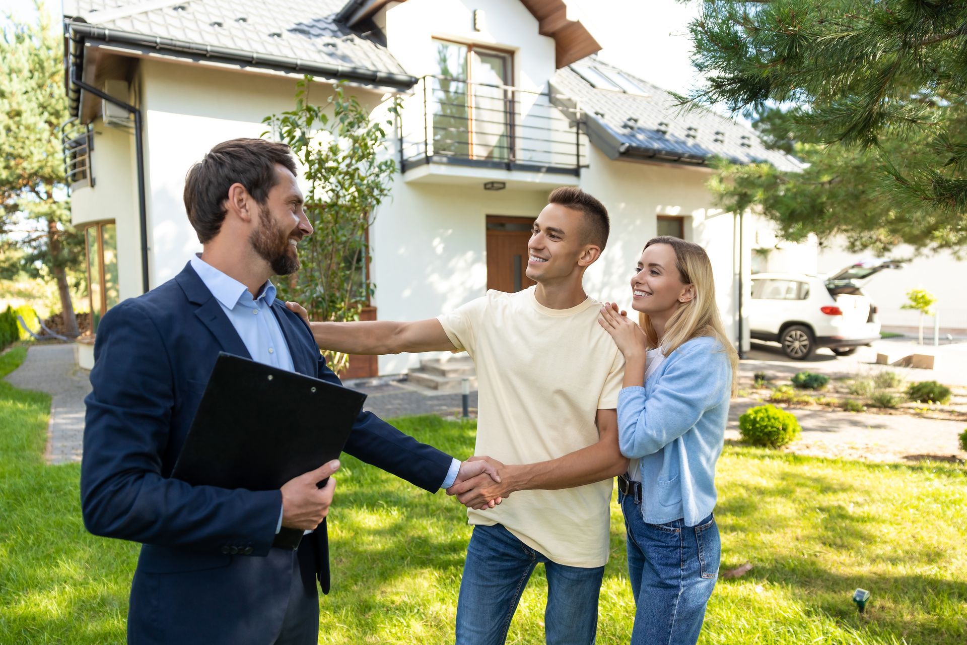 Real estate agent shaking hands with a couple outside a house on a sunny day