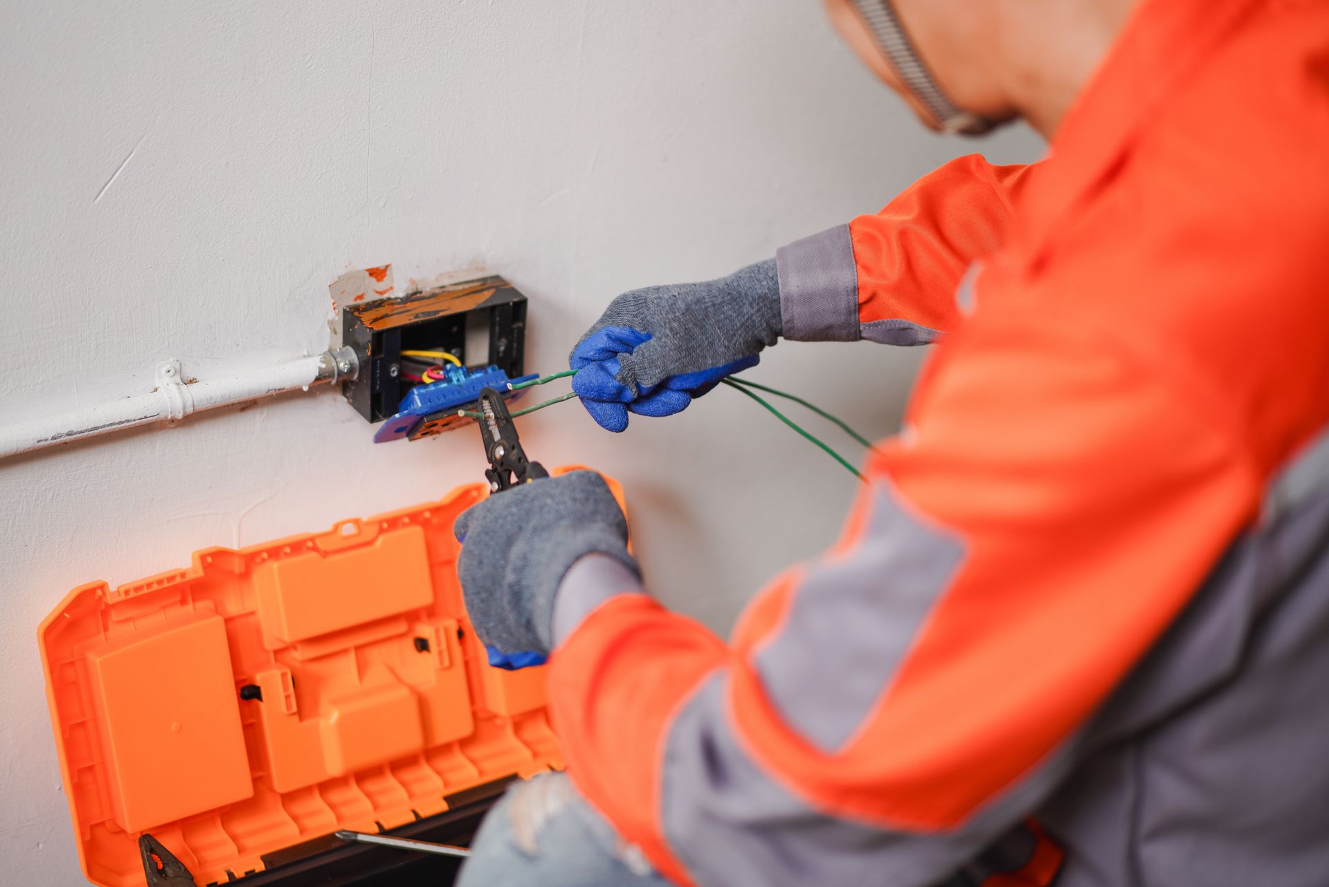 Technician in orange safety gear wiring an electrical box with tools nearby