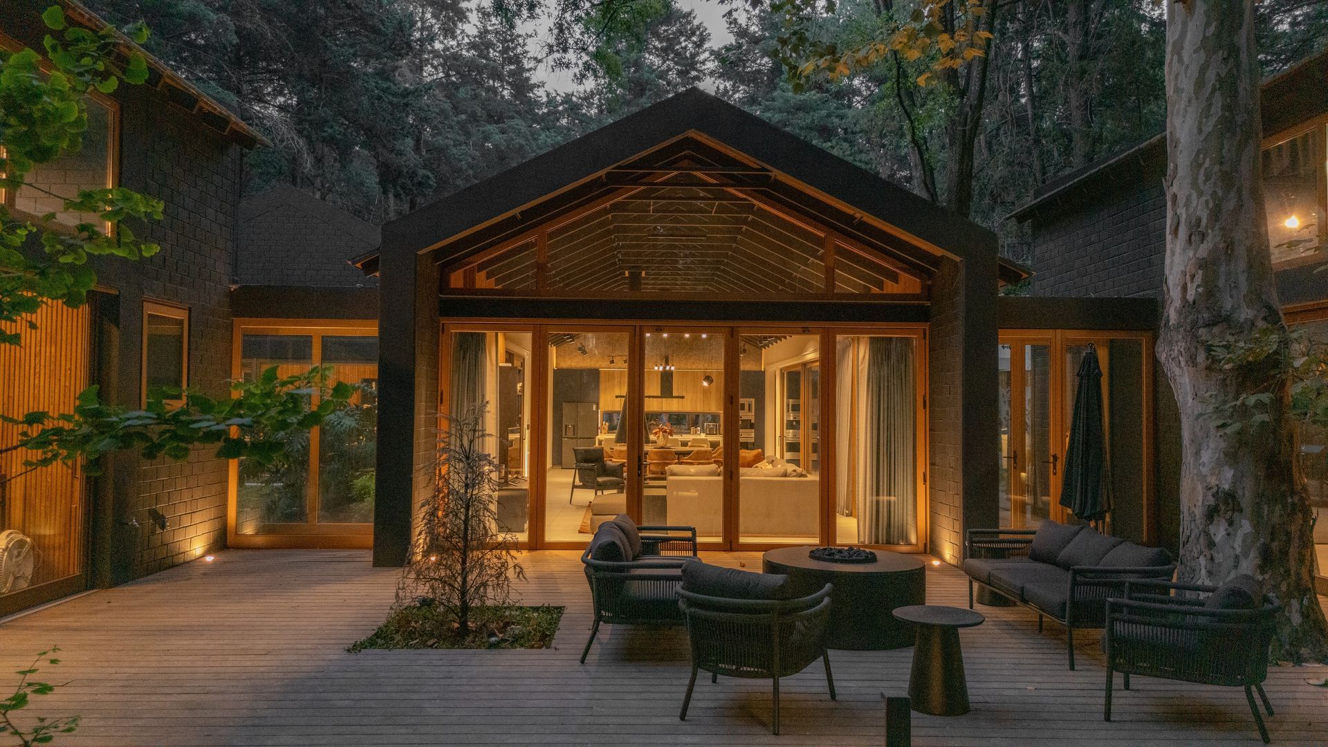 Cozy cabin courtyard at dusk with warm lights, wicker seating, and tall trees surrounding the patio.
