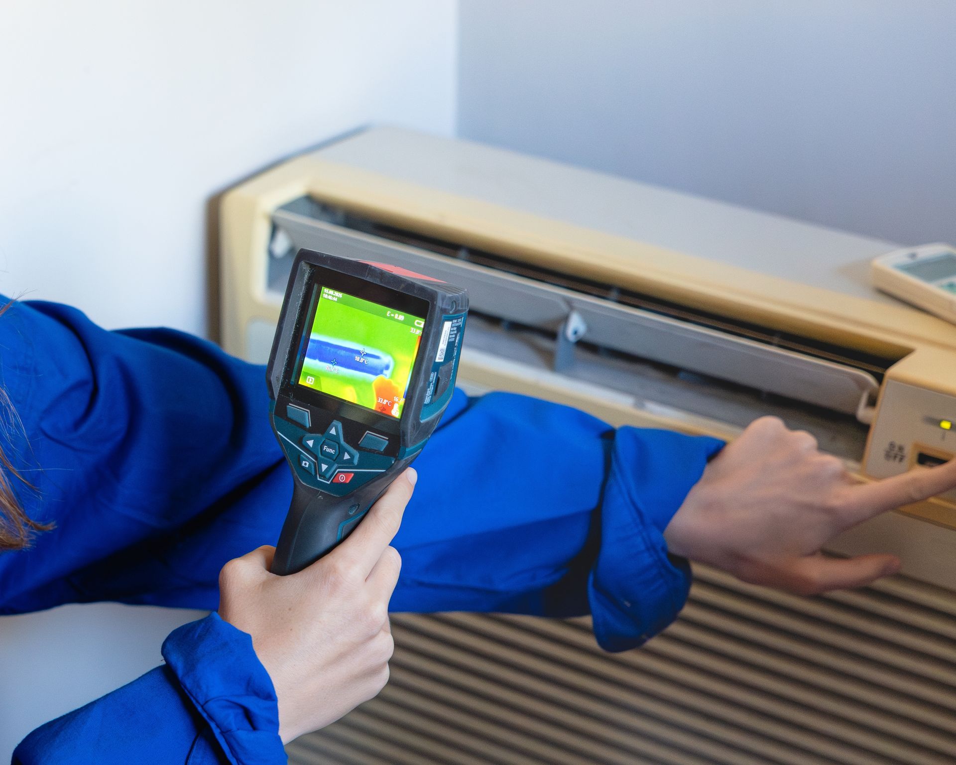 Worker using a thermal camera to inspect an air conditioner unit in a blue jacket.