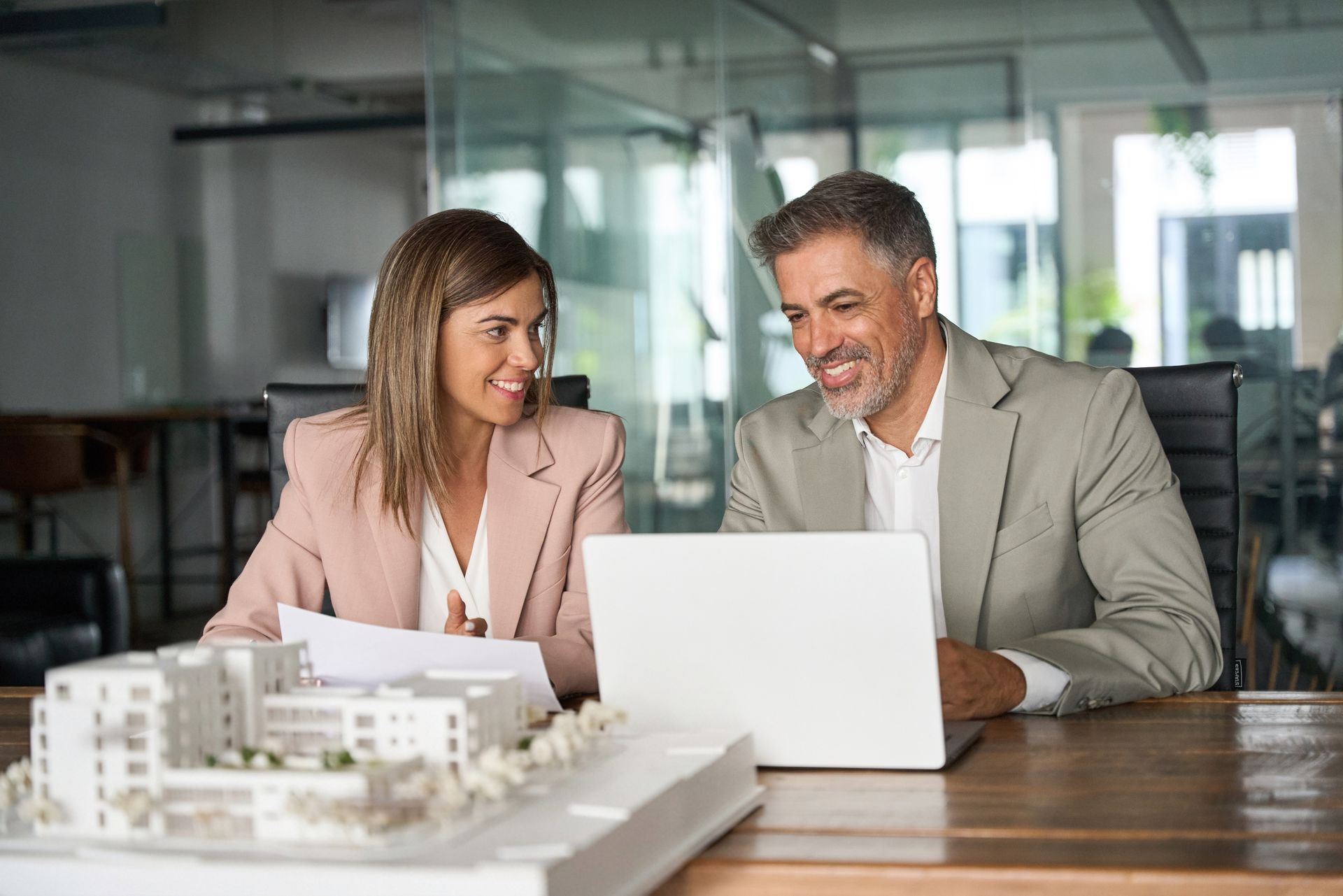 Two business people reviewing a laptop with an architectural model on the table in a modern office