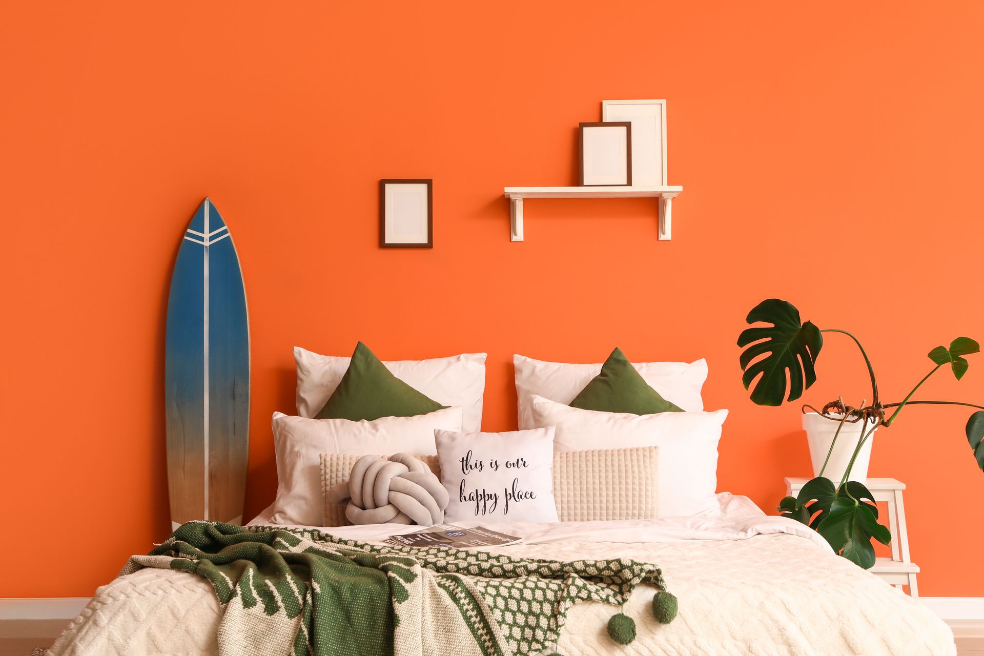 Cozy bed with white bedding, green pillows, and surfboard decor against a bright orange wall.