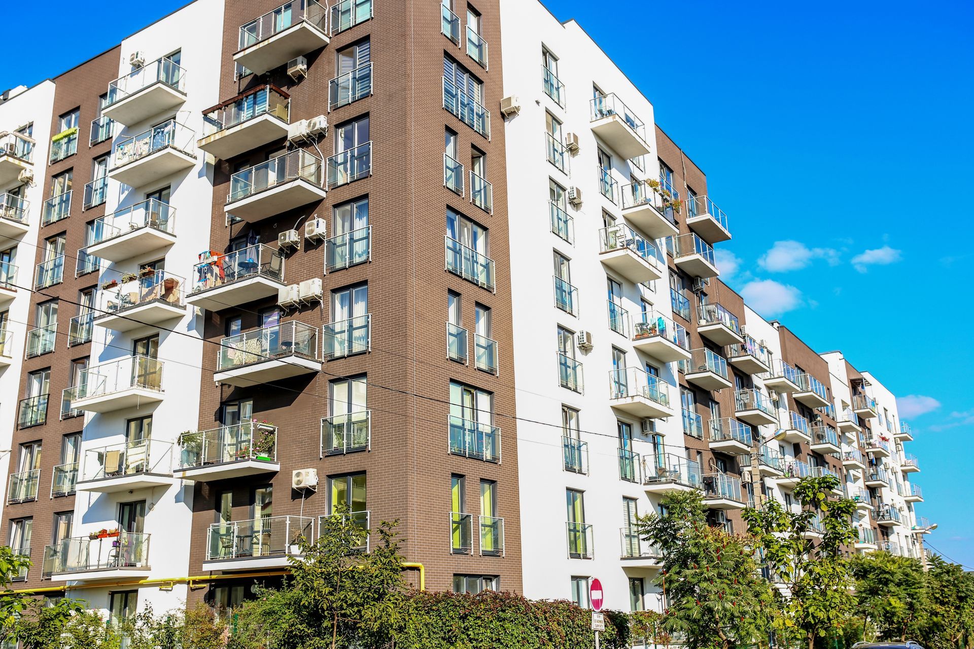 Modern apartment building with balconies, white and brown exterior, under a bright blue sky