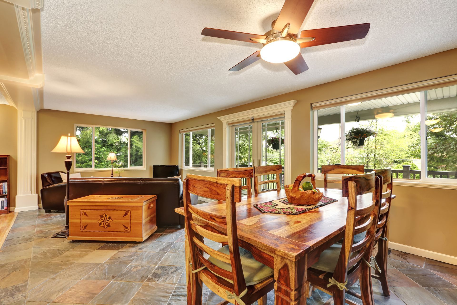 Bright open dining and living room with wood furniture, large windows, and a ceiling fan