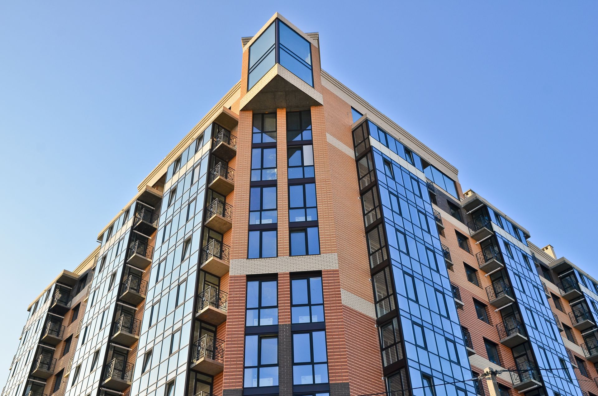 Modern high-rise apartment building with blue-tinted windows and brick exterior against a clear sky