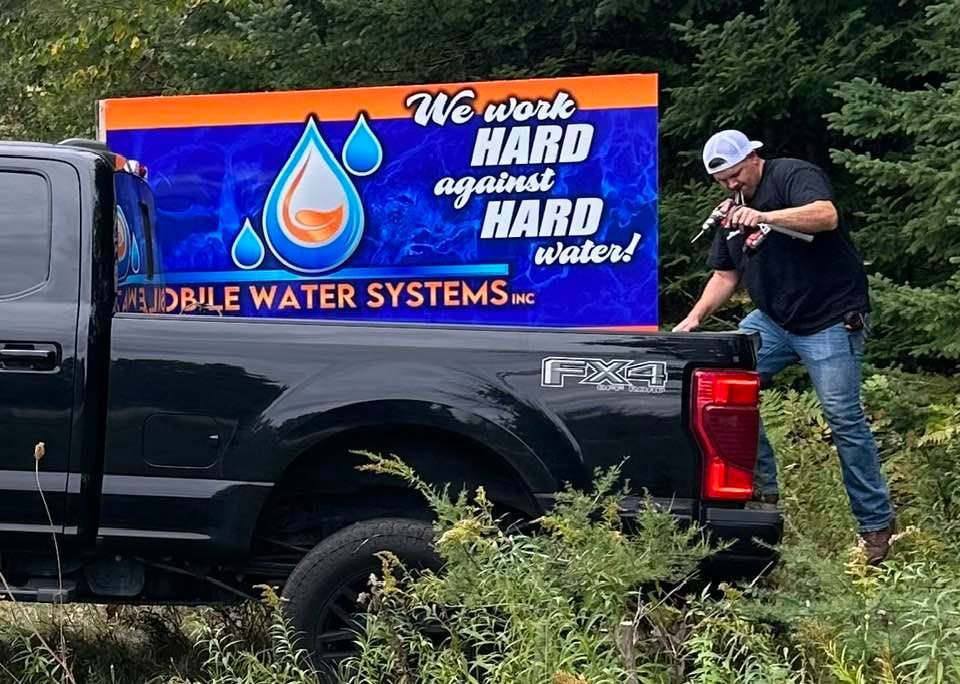 A man is standing next to a truck that says we work hard against hard water.