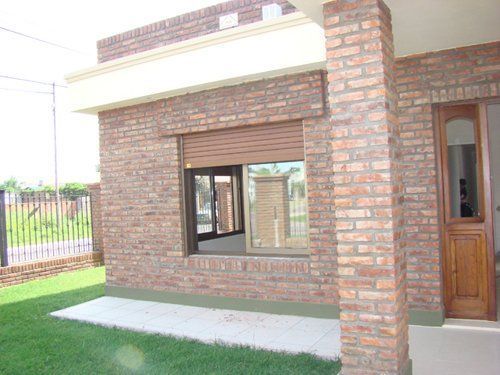 Exterior de una casa de ladrillo con una ventana, una puerta principal y un pequeño jardín.