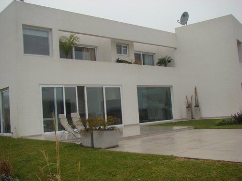 Casa blanca moderna con grandes ventanales, sillas de patio y un patio húmedo en un día nublado