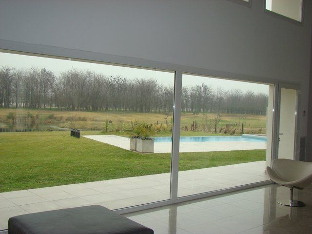 Habitación moderna con grandes puertas acristaladas que dan a un césped y a una piscina rectangular bajo un cielo nublado