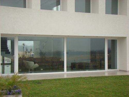 Exterior de una casa moderna con grandes puertas correderas de cristal que dan a un jardín con césped