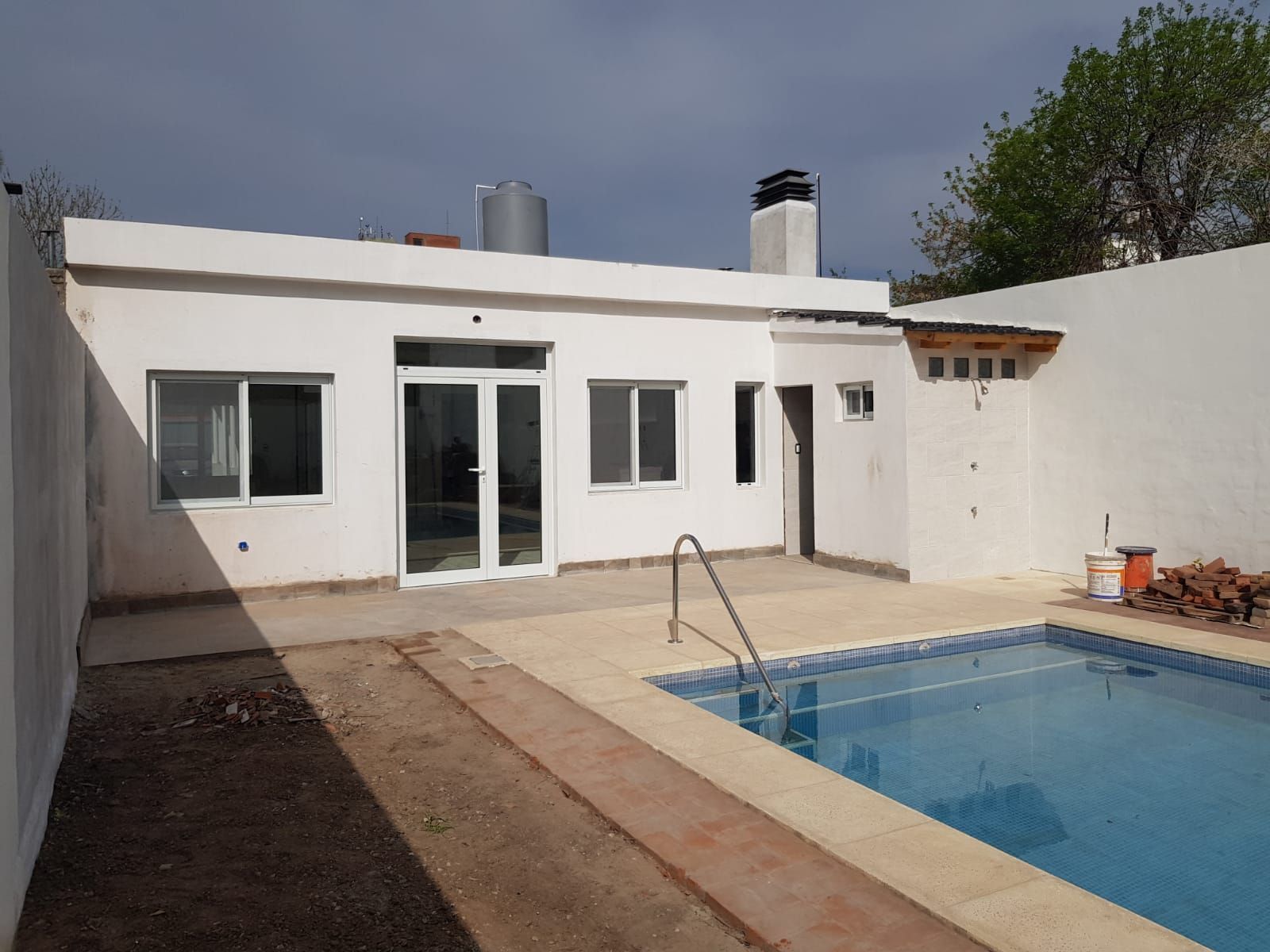 Patio de la Casa Blanca con una pequeña piscina azul y puertas corredizas de cristal bajo un sol radiante