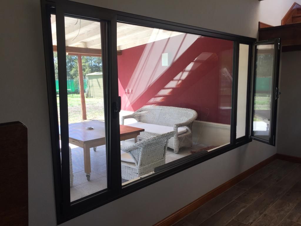 Vista del patio a través de grandes puertas corredizas de vidrio que dan a una habitación de paredes rojas con sillas y una mesa.