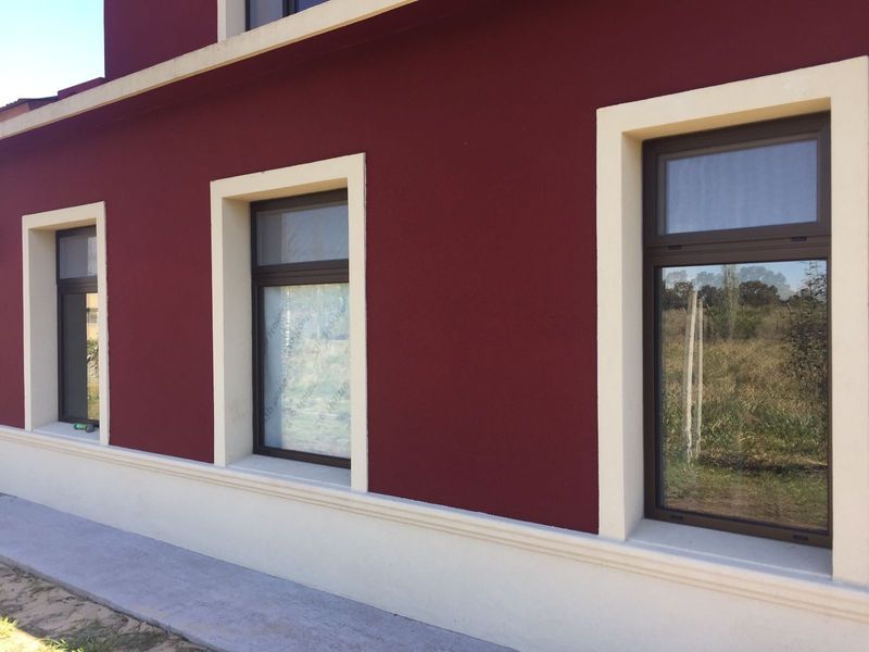 Fachada de edificio granate con tres ventanas enmarcadas en color crema y una base de estuco claro, junto a una acera