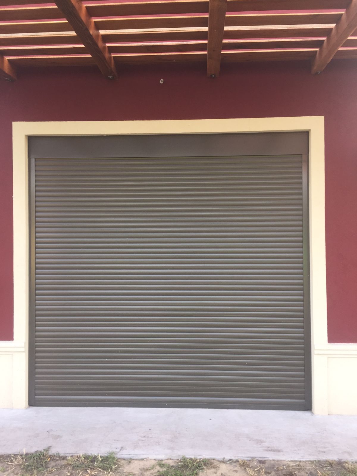 Puerta enrollable gris cerrada en un edificio rojo con molduras blancas y un porche cubierto.