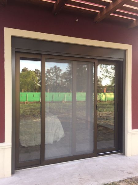 Puerta corredera de vidrio para patio, con marco oscuro y molduras color crema, en una pared exterior granate