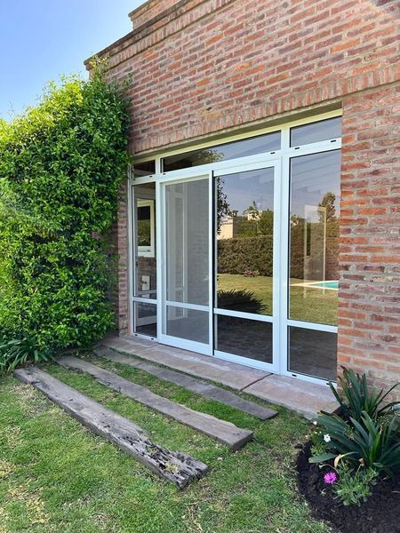 Patio de una casa de ladrillo con puertas corredizas de vidrio, un arbusto verde y dos tablones de madera en el suelo