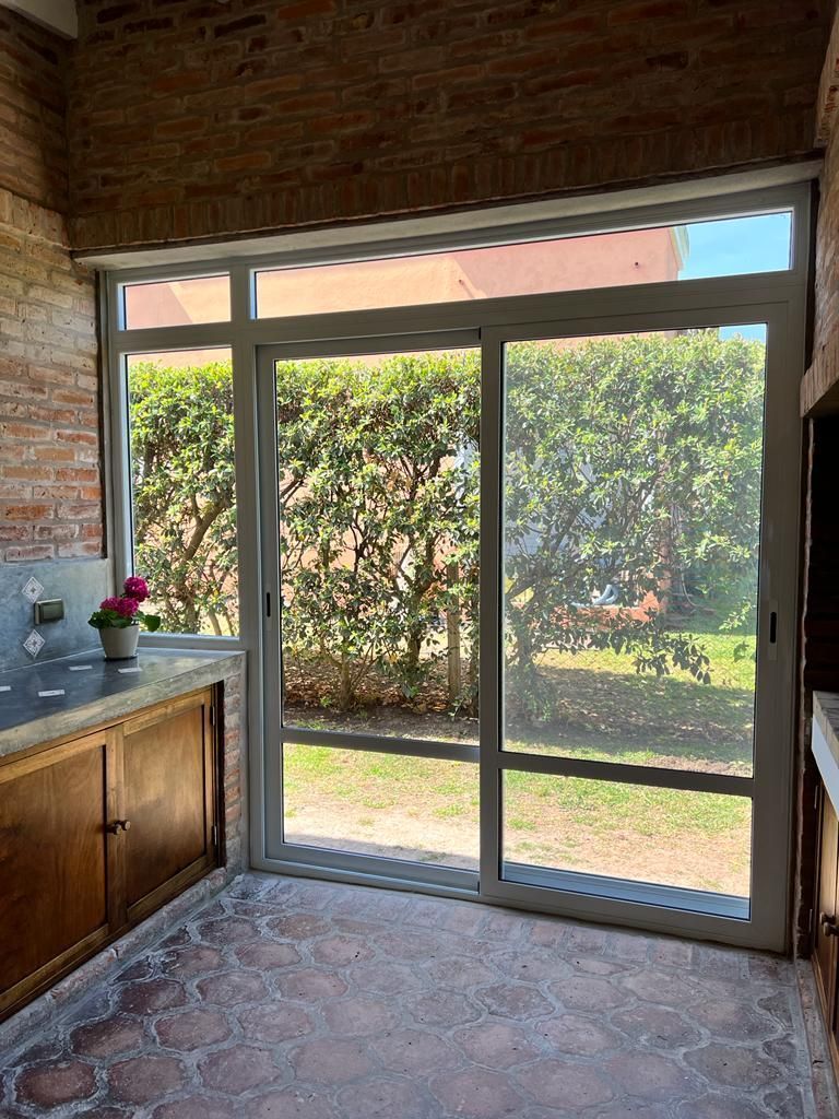 Cocina con suelo y encimera de azulejos, con acceso a una puerta corredera de cristal con mosquitera y a un jardín frondoso en el exterior