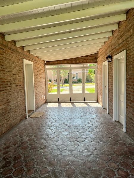 Patio cubierto de ladrillo con suelo de baldosas estampadas, puertas blancas a ambos lados y puertas de cristal que dan a un jardín soleado.