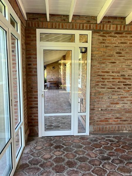 Porche cubierto de ladrillo con puerta exterior acristalada con marco blanco y suelo de baldosas estampadas