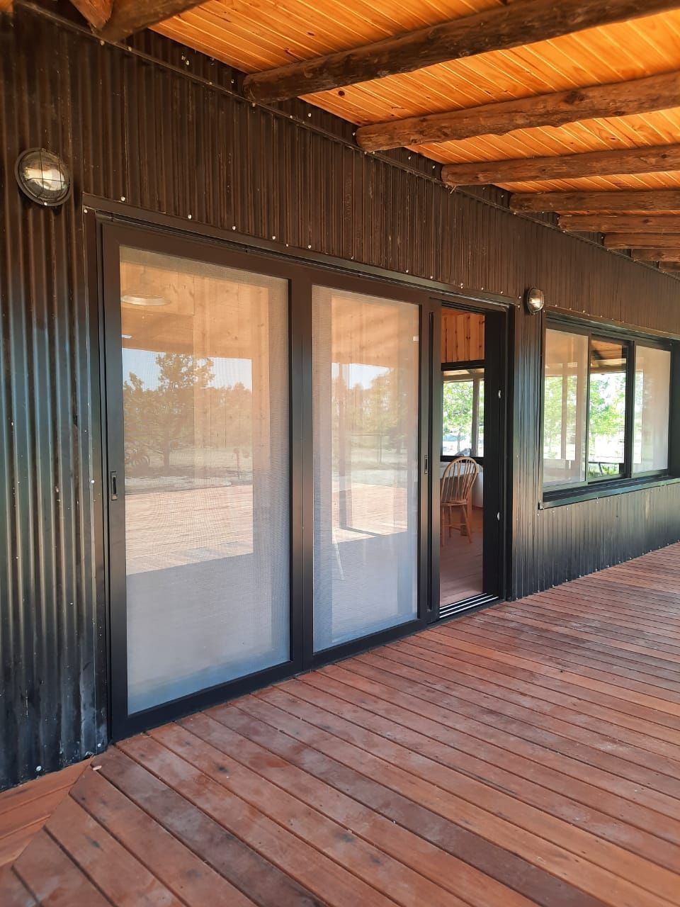 Edificio de metal corrugado negro con puertas corredizas de vidrio y un porche de madera bajo un techo cubierto