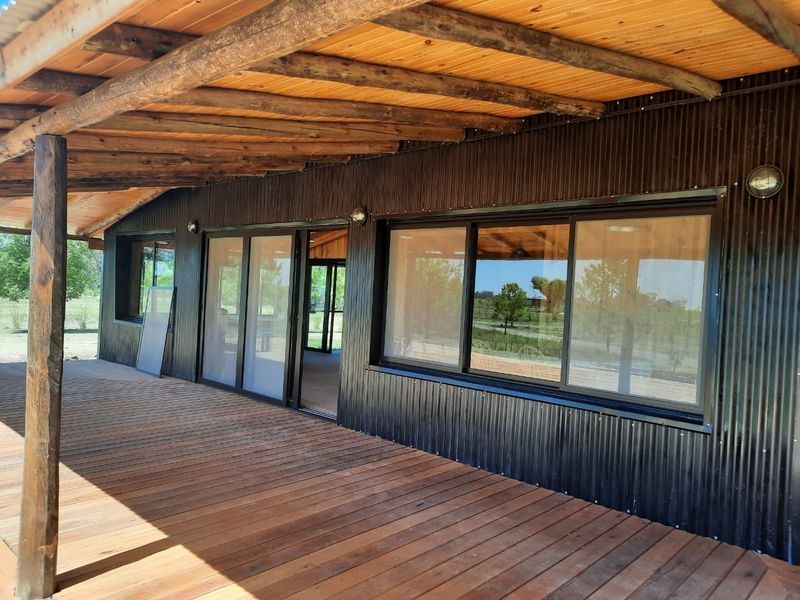 Porche cubierto de madera junto a un edificio rústico con revestimiento negro, grandes ventanas y puertas corredizas de cristal.