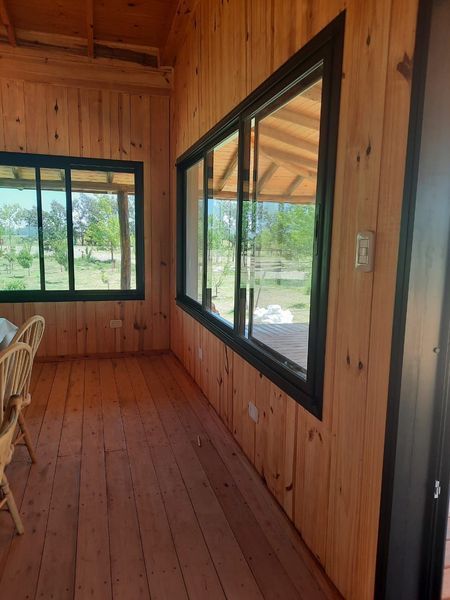 Sala revestida de madera con grandes ventanales de marcos negros que dan a un paisaje verde.