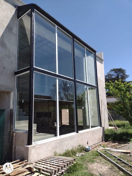 Ampliación moderna de una casa de cristal, con grandes ventanales de suelo a techo y una base de hormigón, al aire libre
