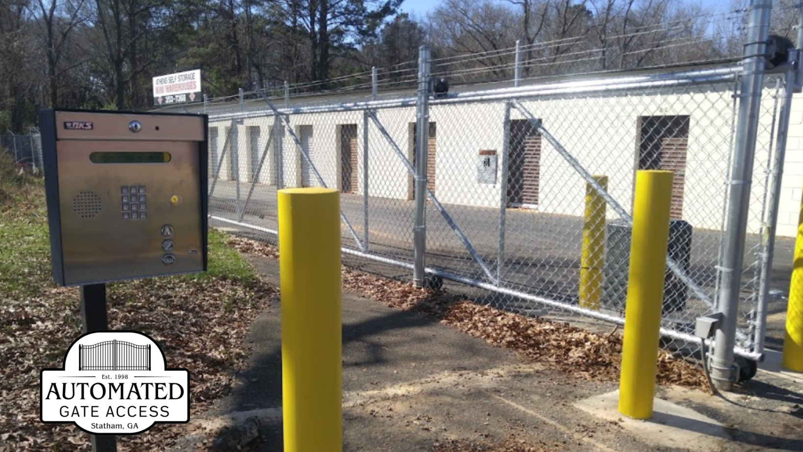 Automated gate with keypad for storage unit access, yellow bollards, chain-link fence.