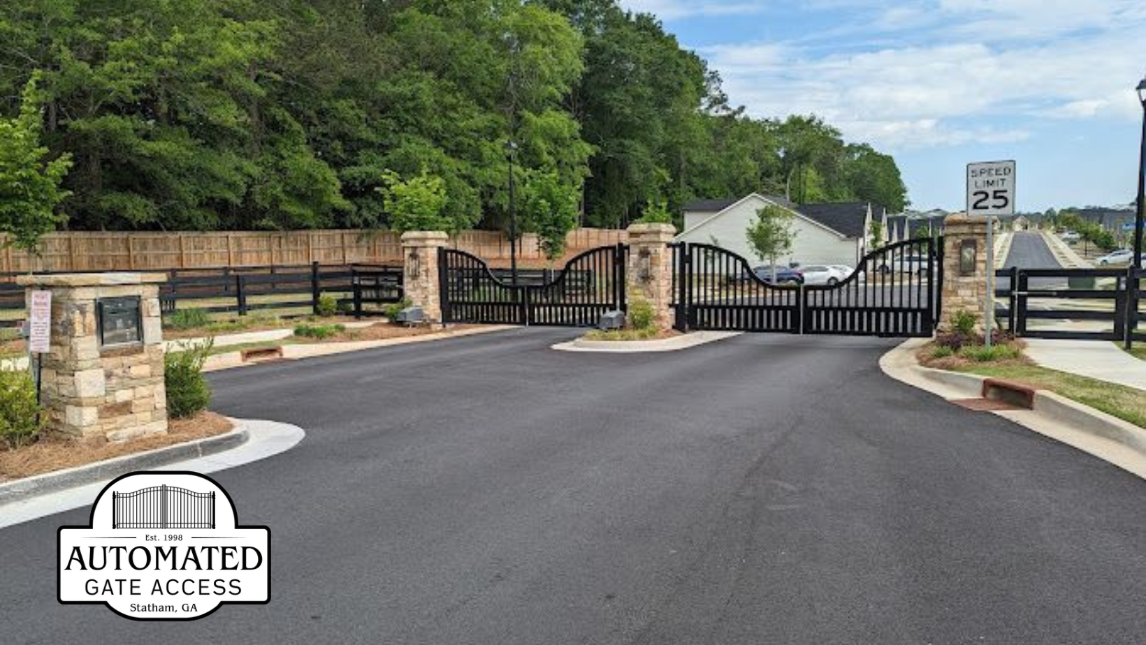 Entrance to gated community with black iron gates, stone pillars, and speed limit sign.