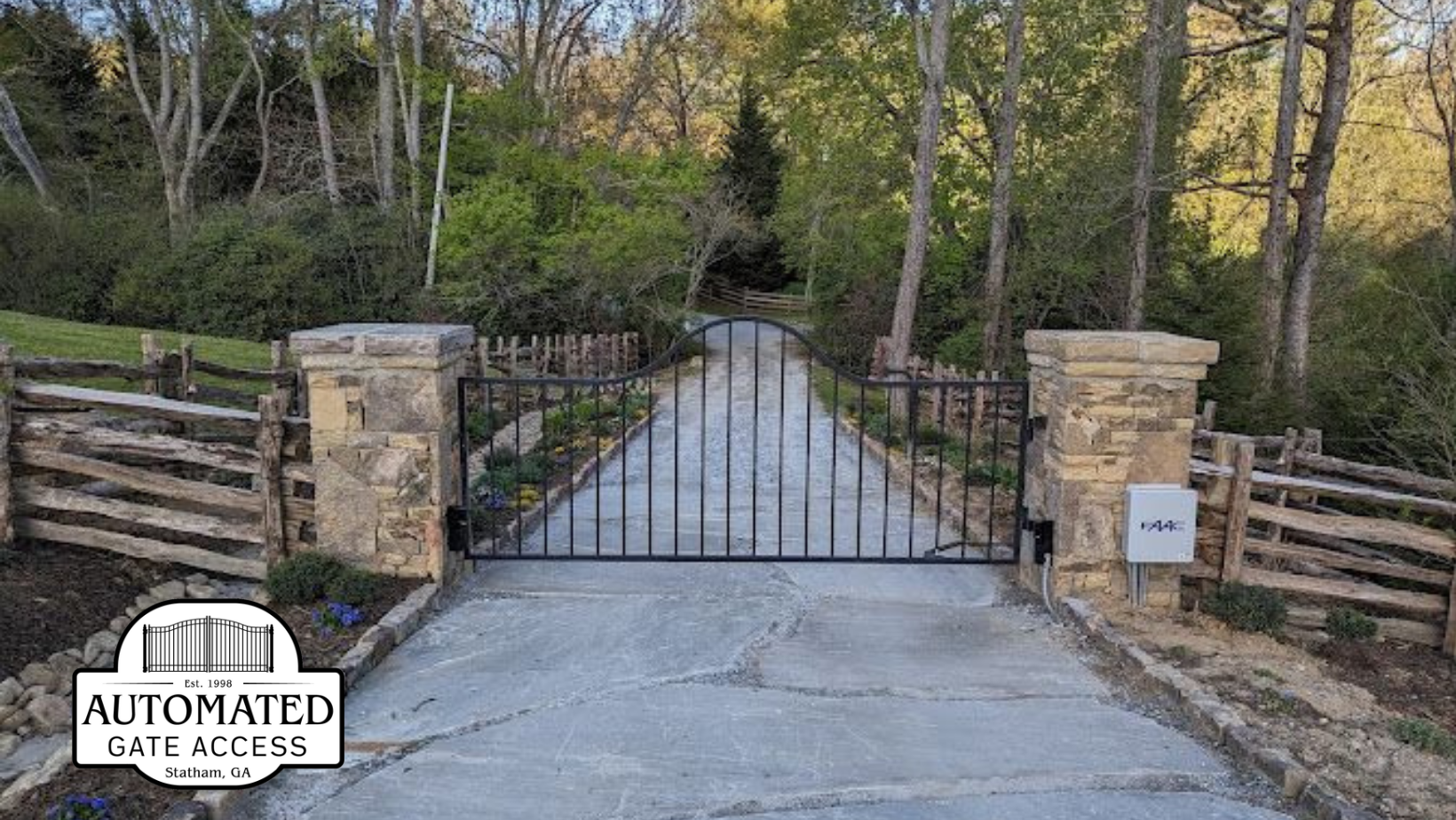 Black automatic gates at entrance to a residential area. Stone pillars with a speed limit sign.