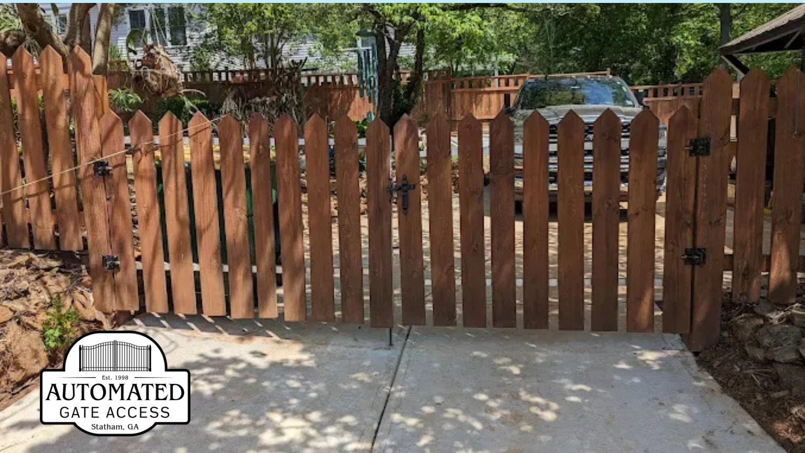 Wooden picket gate in front of a concrete driveway, with a car visible in the background.