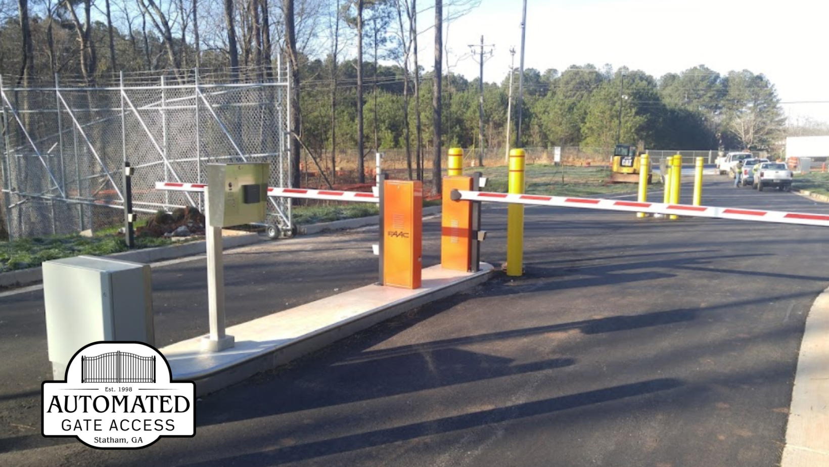 Automated gate with red and white striped arm, orange control boxes, and chain-link fence.