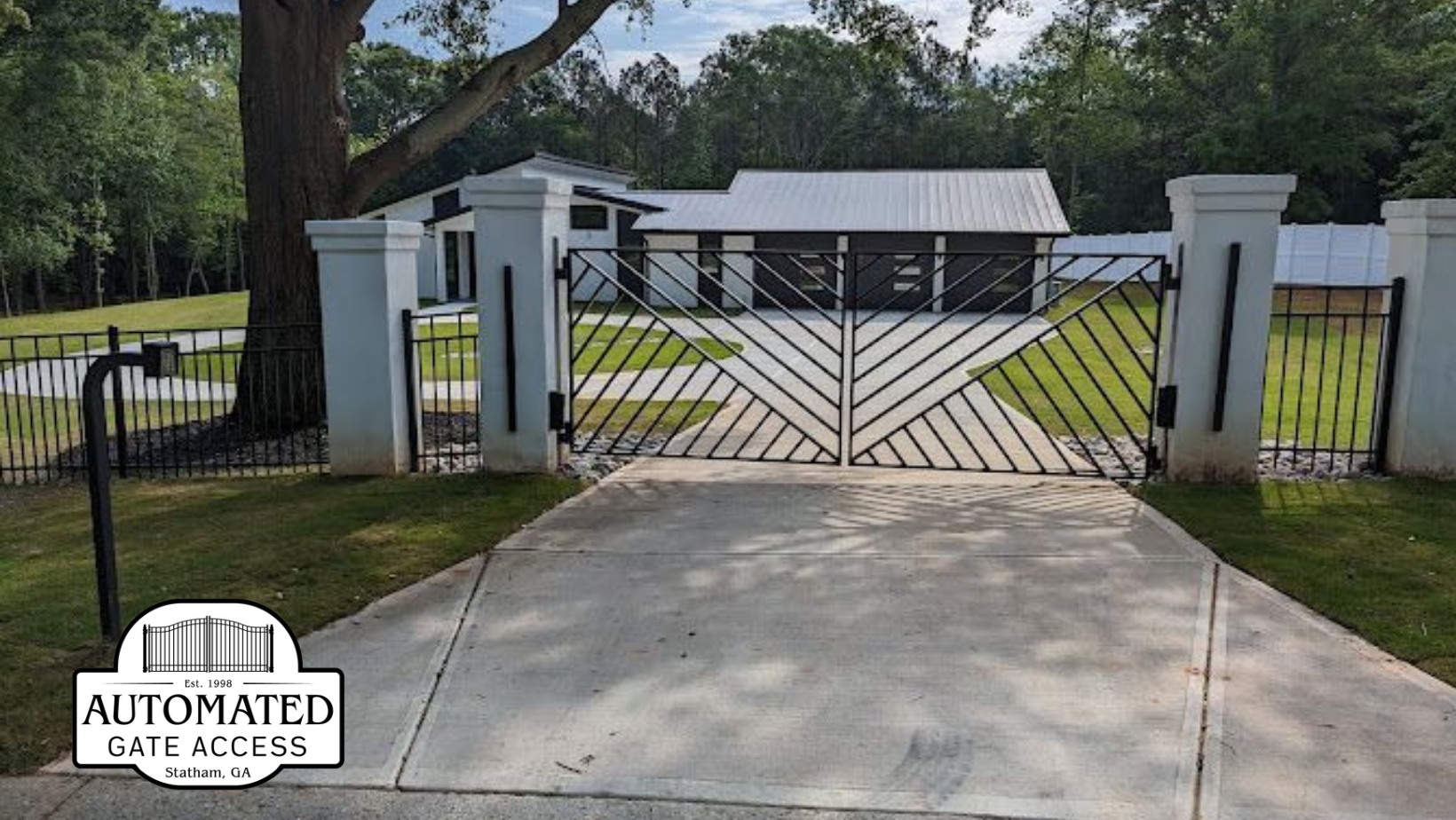 Decorative metal gate and driveway leading to a white house with a metal roof.