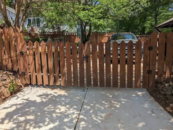A wooden fence surrounds a driveway with a car parked behind it.