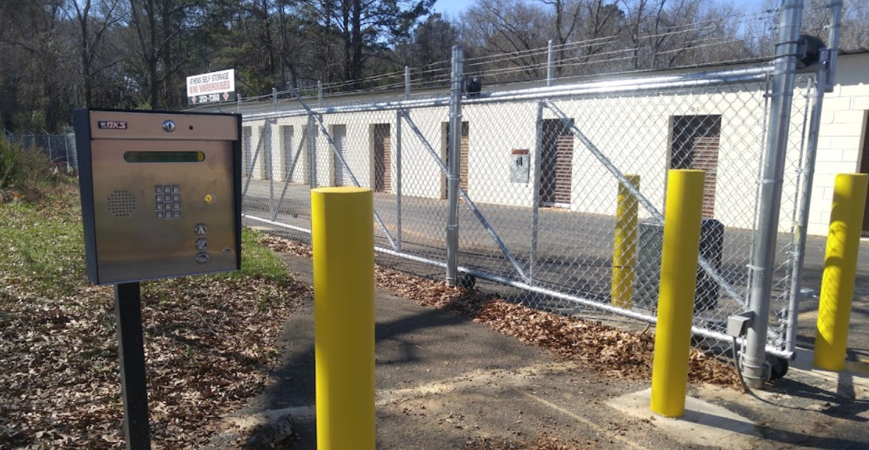 A wooden fence surrounds a driveway with a car parked behind it.