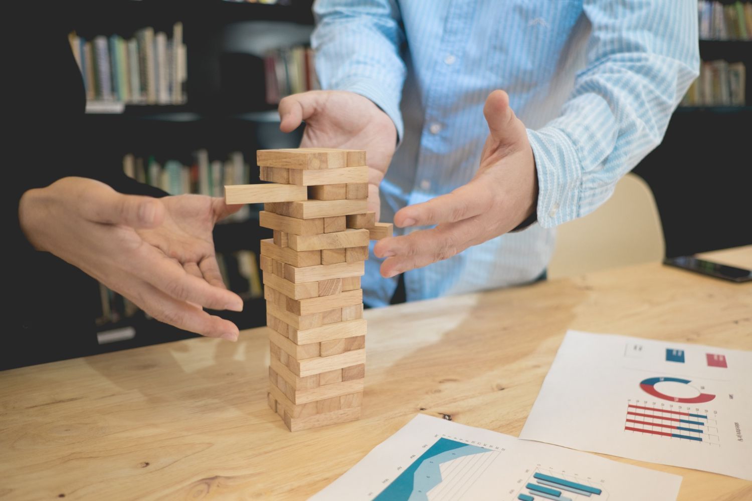 A man and a woman are playing a game of jenga on a wooden table.