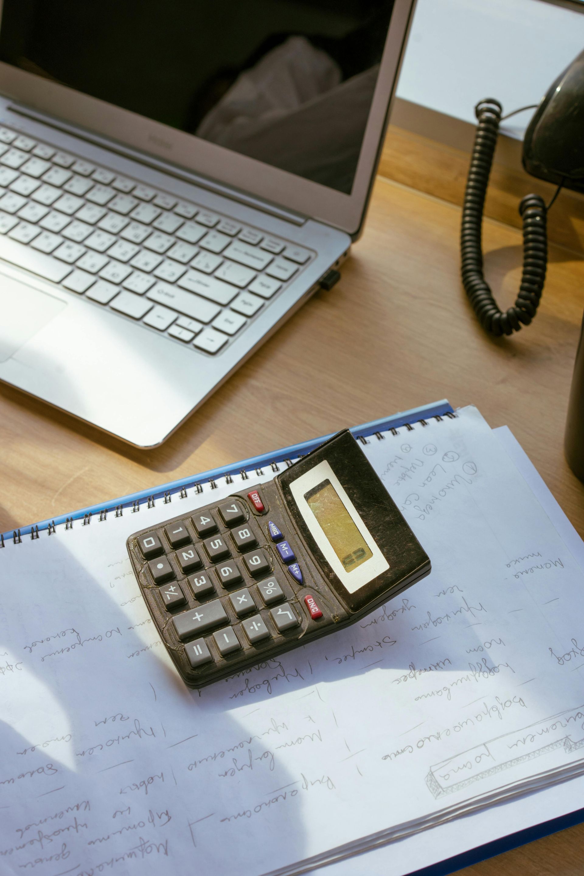 A calculator is sitting on top of a notebook next to a laptop.