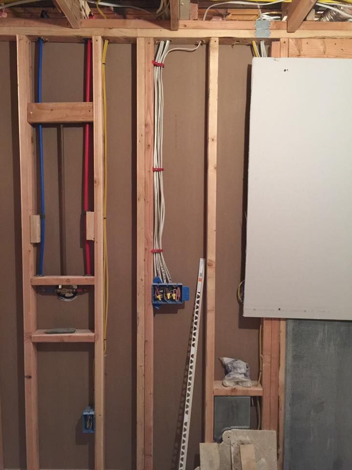 Interior wall framing with plumbing, electrical, and drywall, showing construction progress.