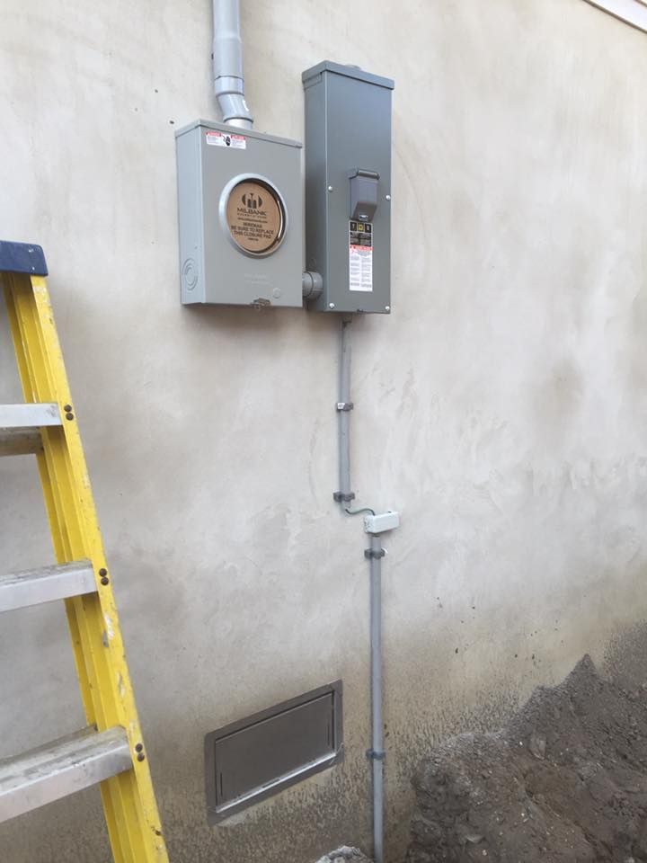 Electrical meter box and panel mounted on a textured wall with conduit running down, ladder to the left.