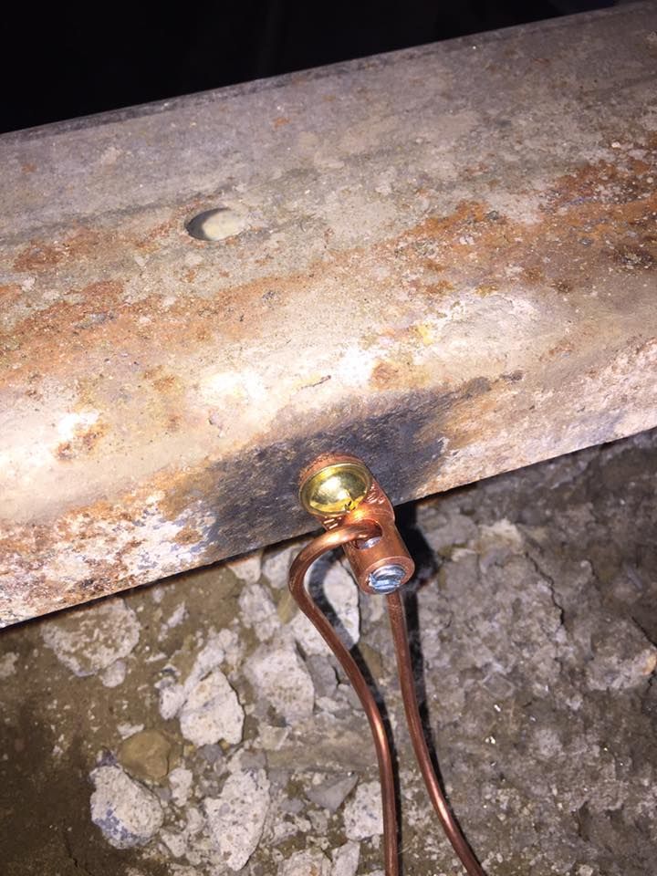 Copper wire connection on rusty metal beam, with dark burn mark.