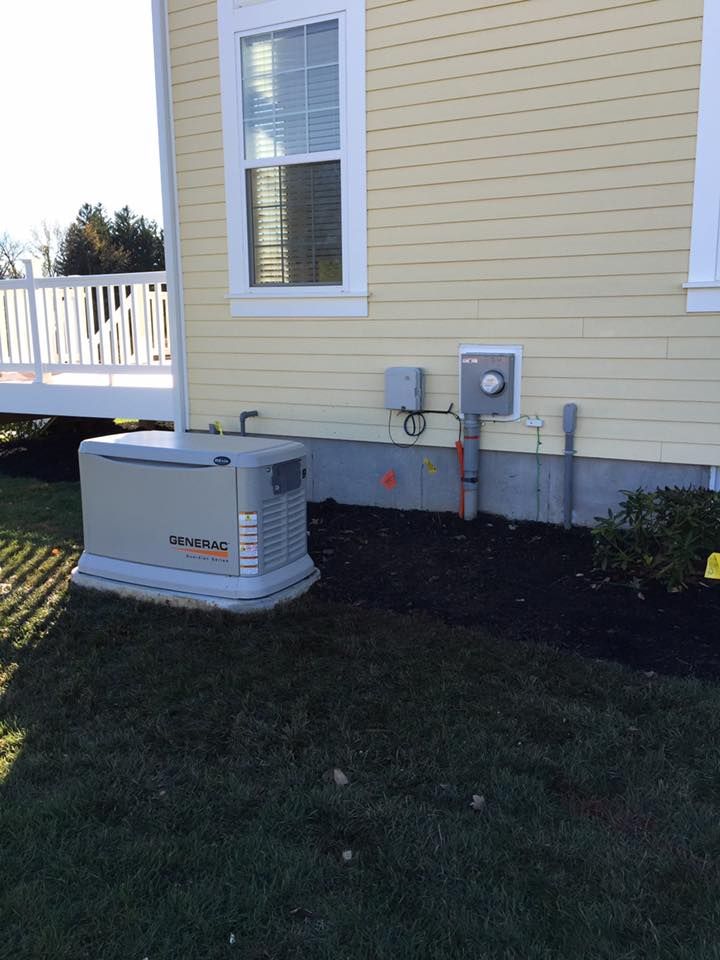 A generator next to a house. Brown, beige and green colors. Electrical box on the wall.