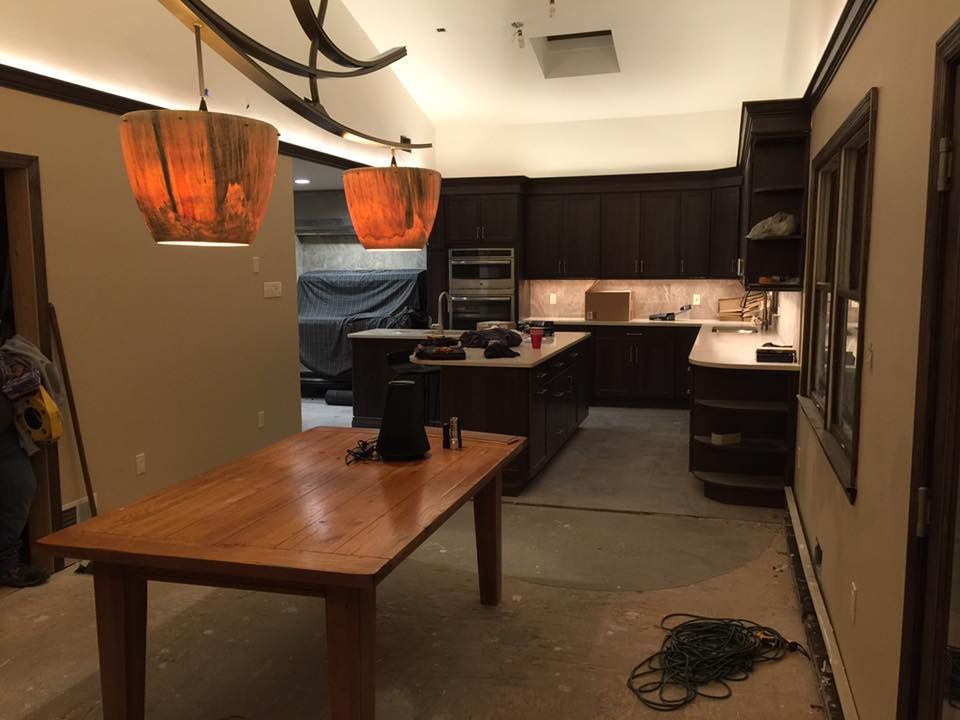 Kitchen remodel in progress: dark cabinets, island, wooden table, pendant lights, construction materials on floor.