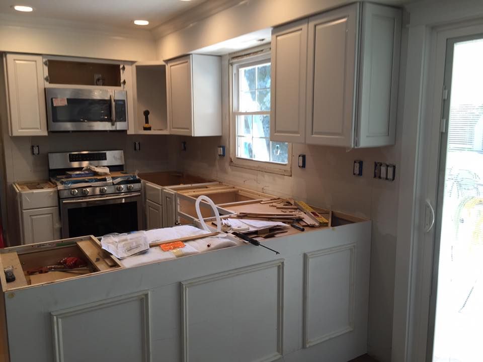 Kitchen undergoing renovation, featuring new white cabinets, appliances, and exposed countertops.