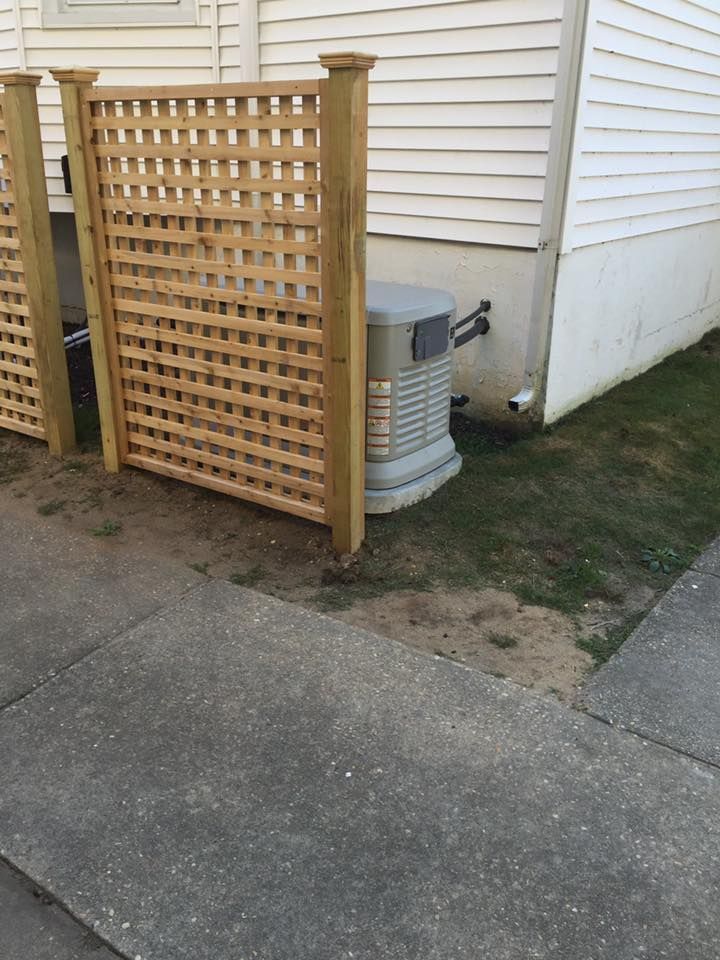 Wooden lattice screen beside a house hides a gray generator.