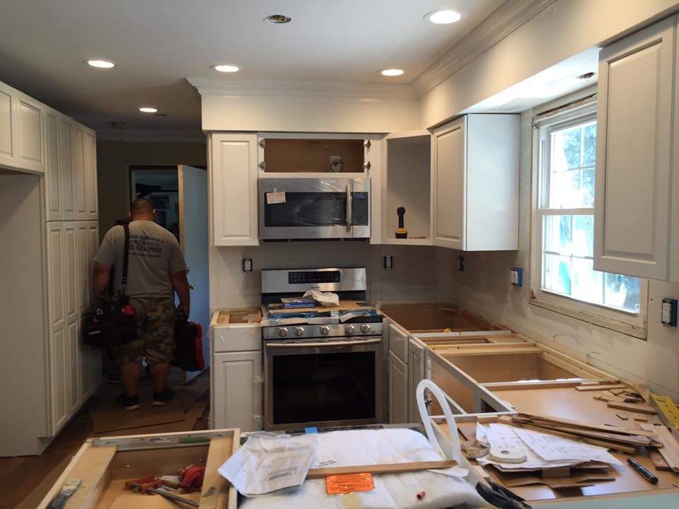 Kitchen under construction, with cabinets, stove, microwave, and a worker carrying a toolbox.